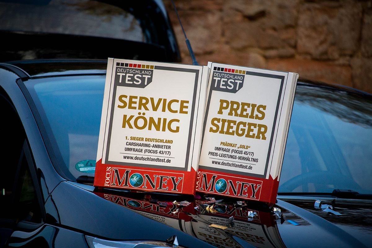 Schwarzes Auto mit zwei Awards von Focus Money auf der Motorhaube, die Flinkster als 'Service König' und 'Preis Sieger' auszeichnen.