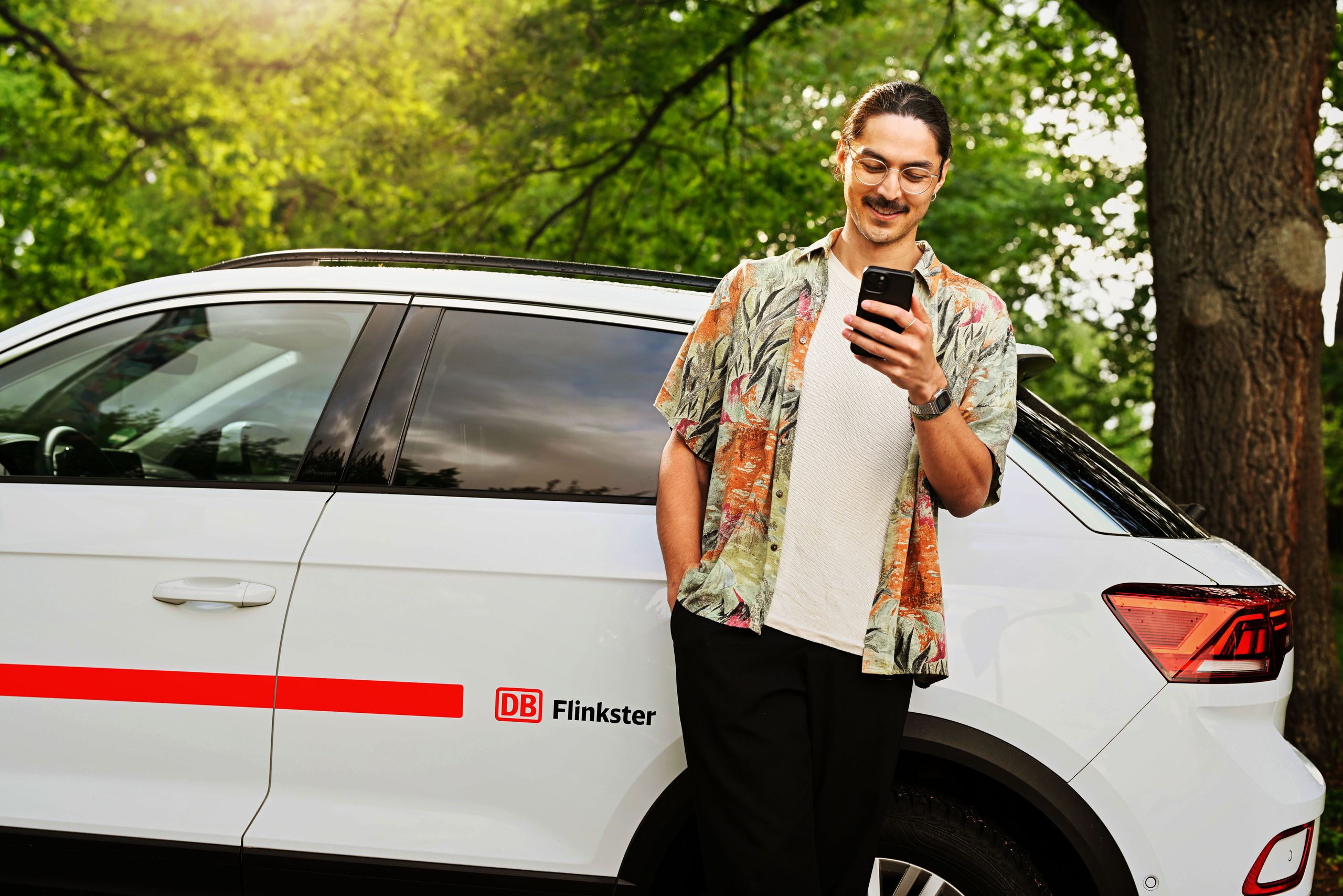erson leaning against a Flinkster car while holding a smartphone
