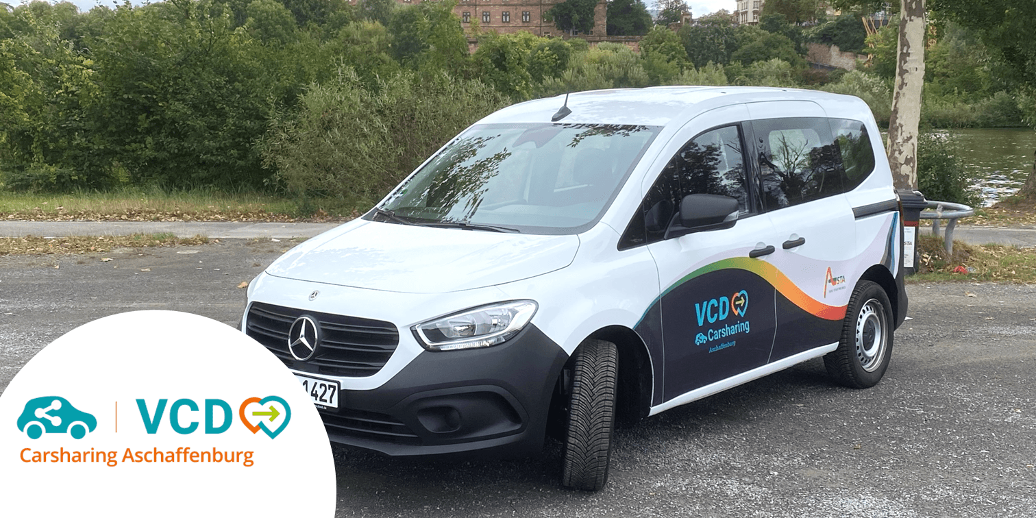 Weißes Mercedes Citan Fahrzeug vom Carsharing Anbieter VCD Aschaffenburg auf Parkplatz vor einem Park und im Hintergrund Bäume, Teich und die Burg von Aschaffenburg.