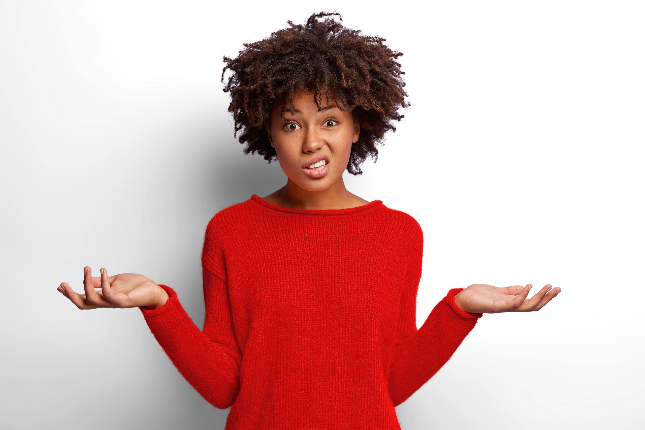 Woman with red top and brown curly hair holds both hands sideways with palms up and a questioning look on her face.