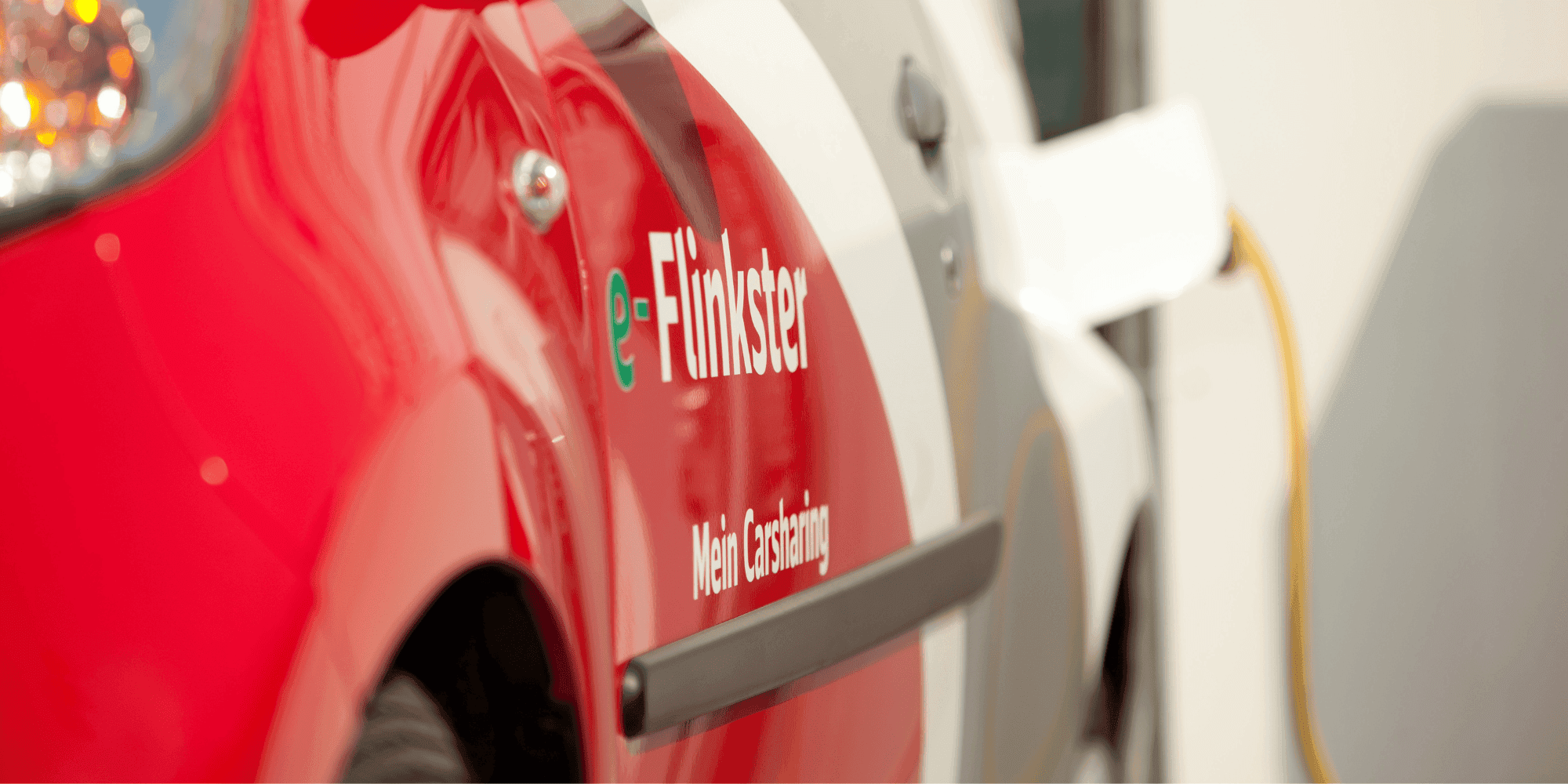 Close-up of a red and white electric car from Flinkster with the lettering 'e-Flinkster' and a charging cable. copyright DB AG / Holger Peters