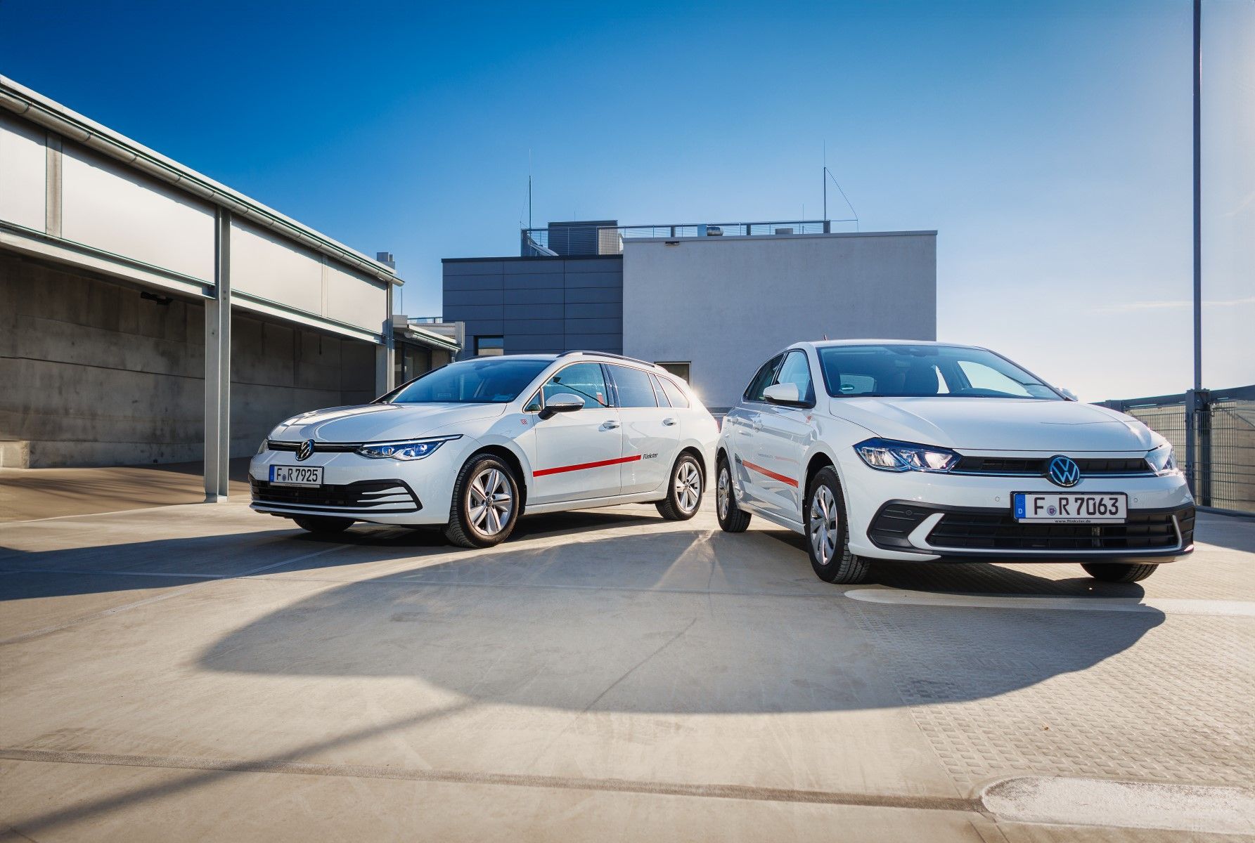 Two white VW vehicles are parked next to each other in a parking lot in sunny weather. Both cars have red stripes and are marked with the words 'Flinkster'.