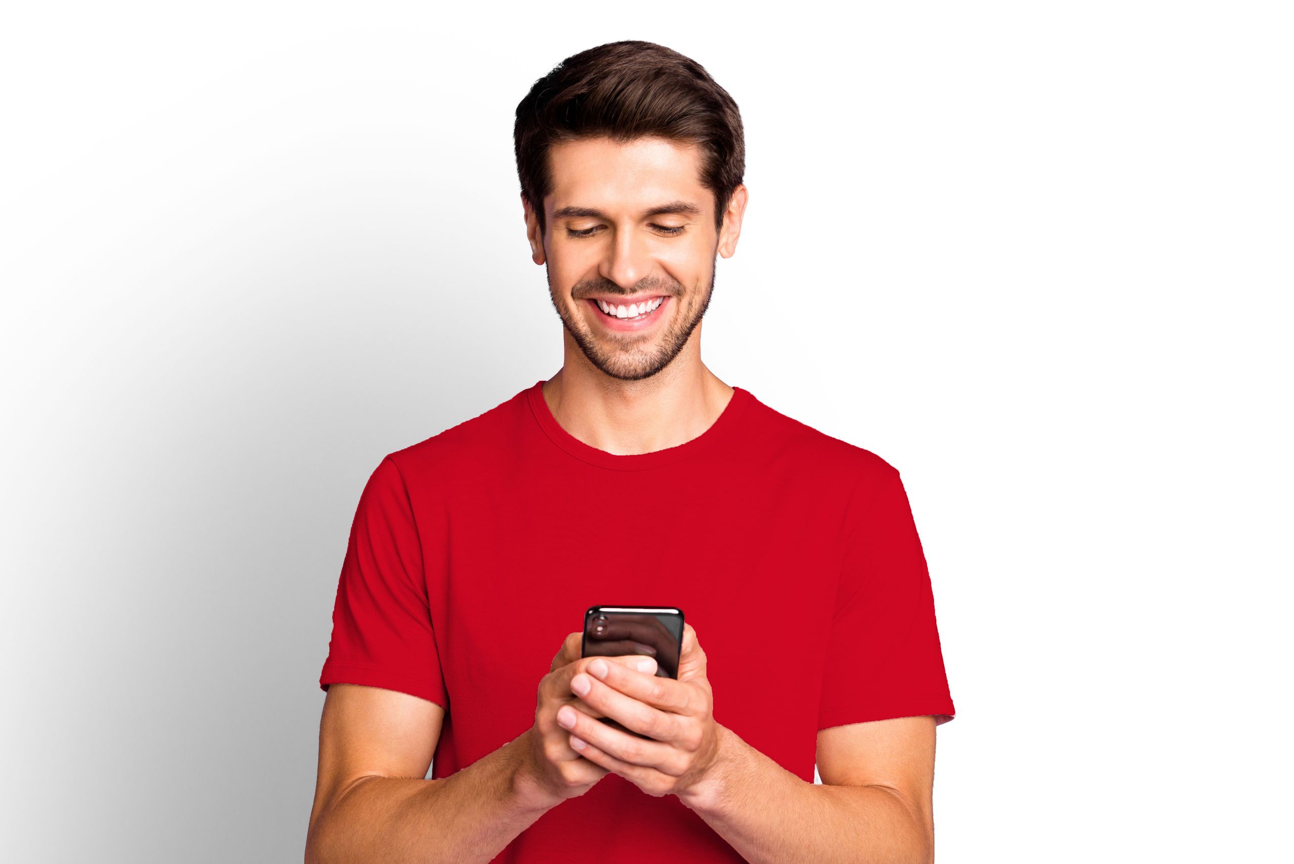 A young man in a red T-shirt smiles as he looks at his smartphone.