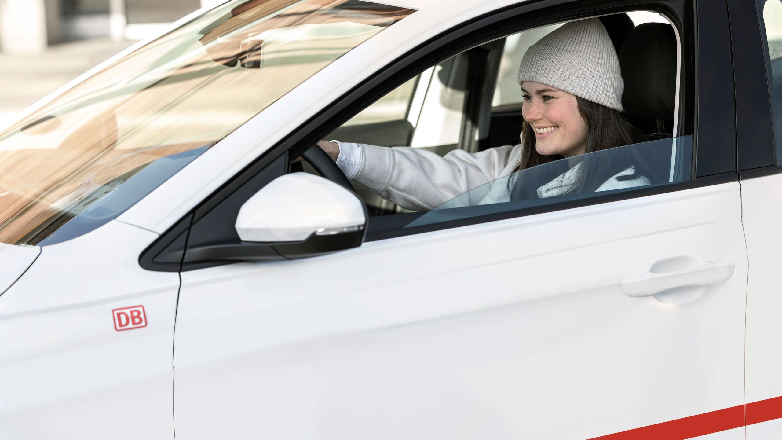 Flinkster customer in a white Flinkster car, smiling and with both hands on the steering wheel.
