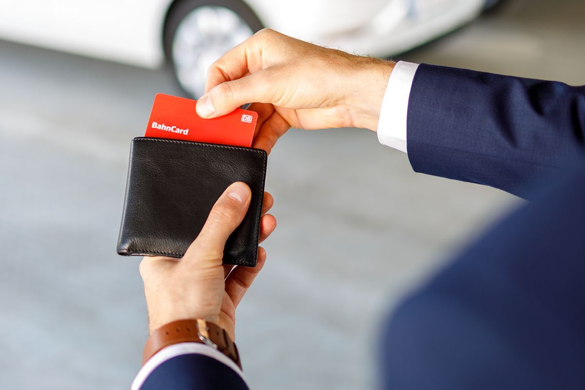 Close-up of hands inserting a BahnCard into a black wallet, with a blurred car in the background.