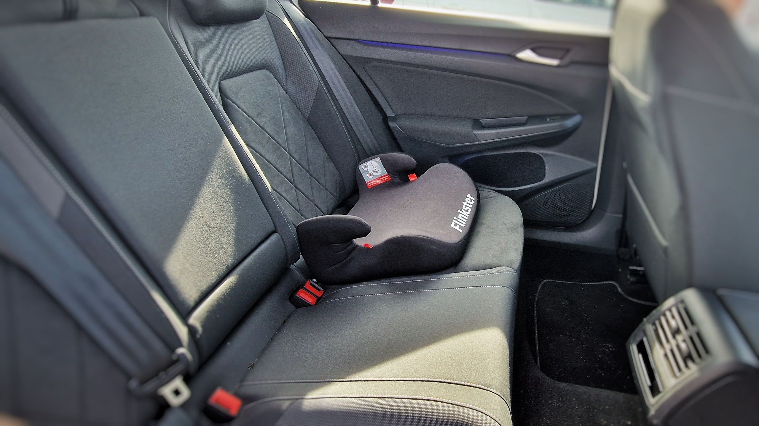 Car interior shows a booster seat in the back seat.
