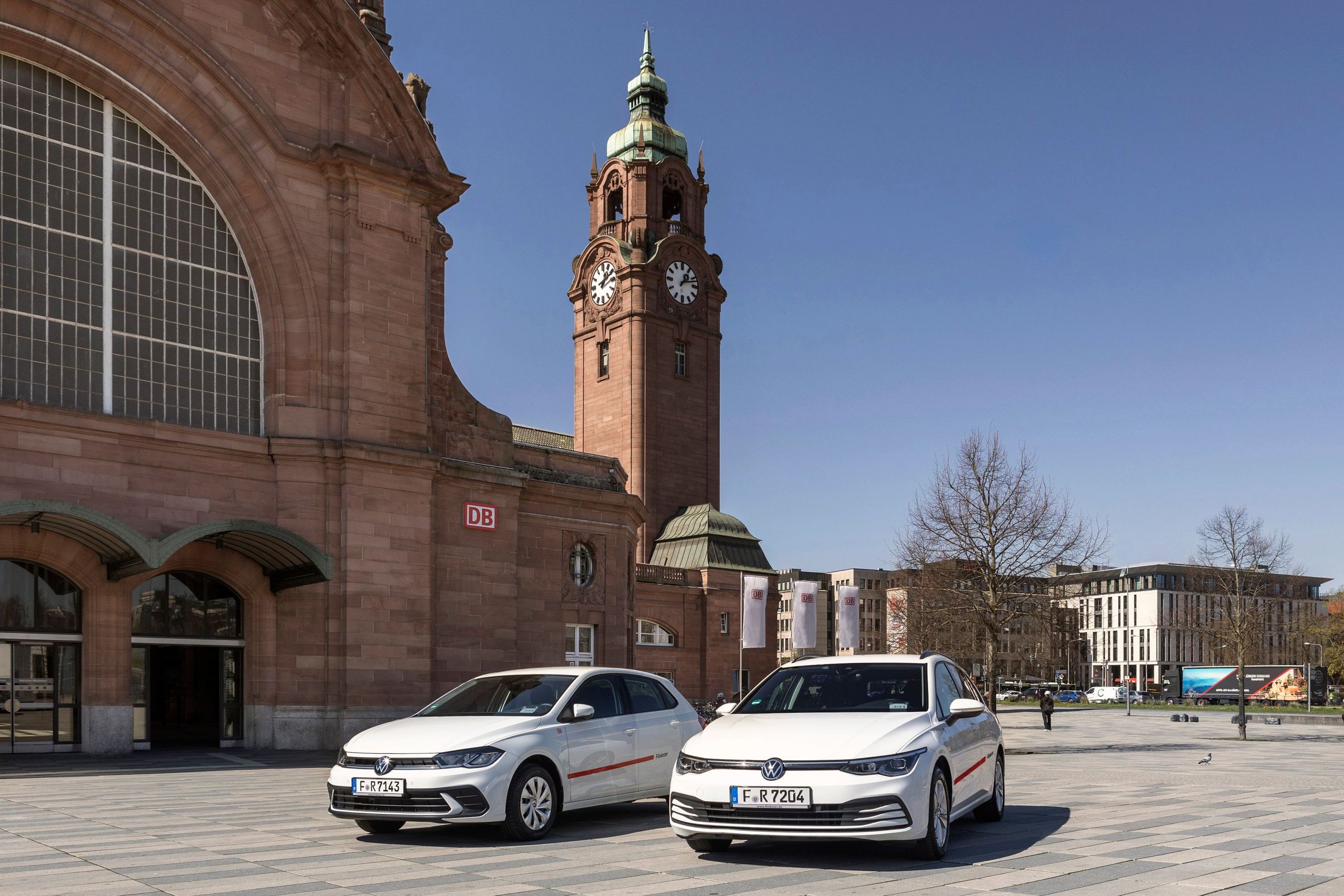 Two white Flinkster cars in front of a historic passenger building with a clock tower and DB logo on a sunny day. copyright Deutsche Bahn