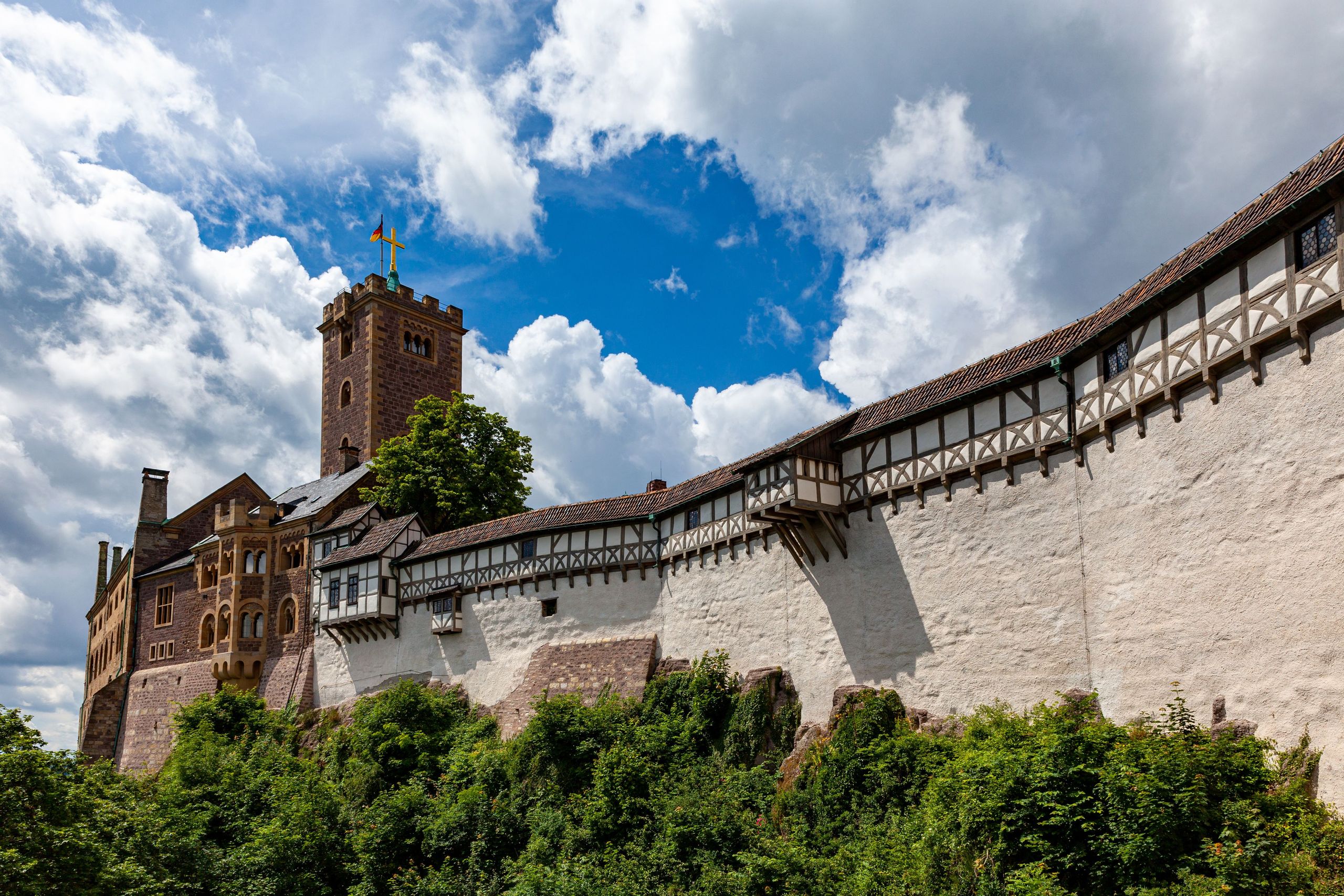 Historische Wartburg mit mehreren Türmen und einem umfangreichen Mauerwerk, die auf einem bewaldeten Hügel steht, unter einem bewölkten blauen Himmel. copyright Foto: istock.com/heckepics