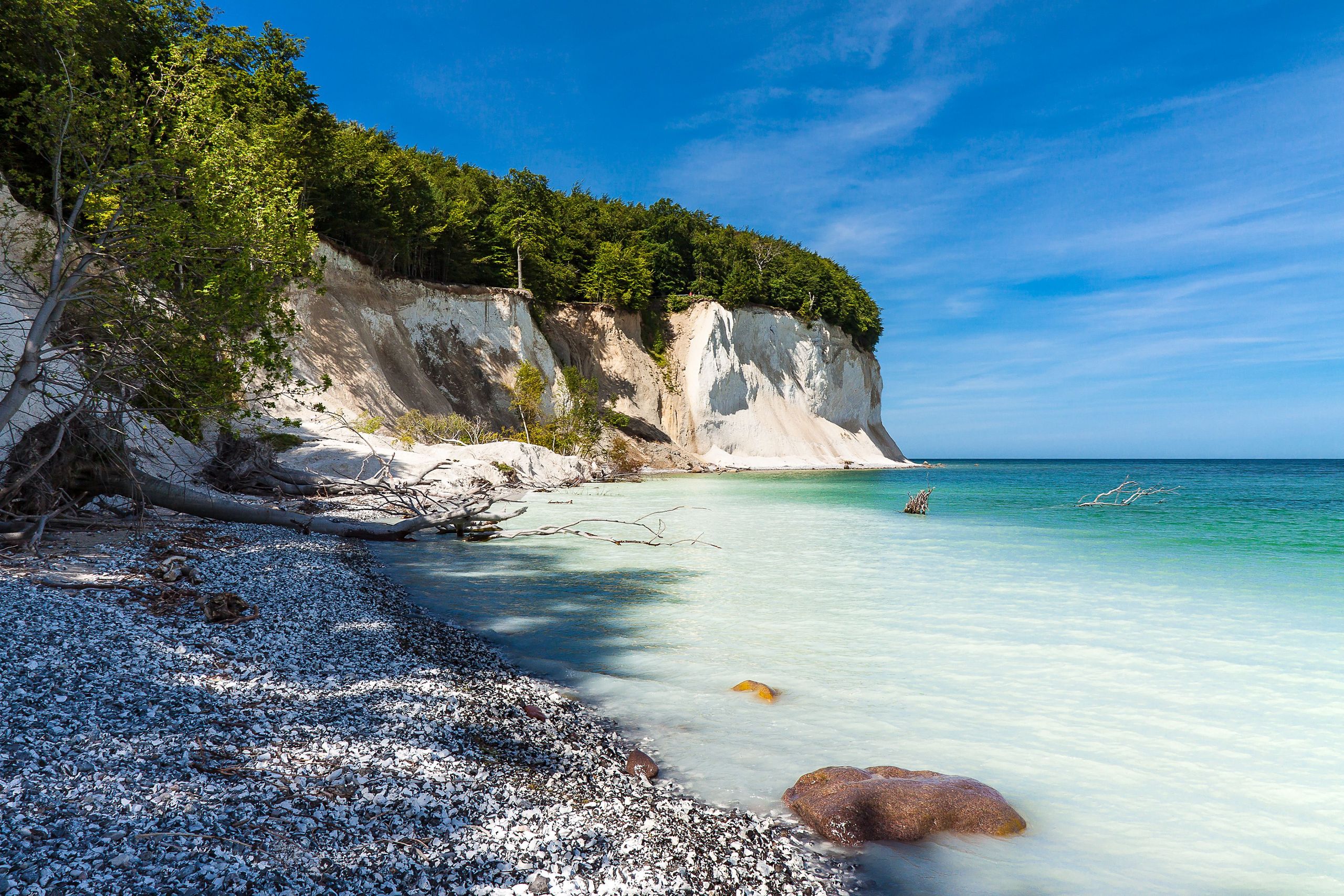 Ansicht eines Strandes auf Rügen mit klarem türkisfarbenem Wasser, weißen Klippen und verstreuten Kieselsteinen am Ufer unter einem klaren blauen Himmel. copyright Foto: istock.com/RicoK69